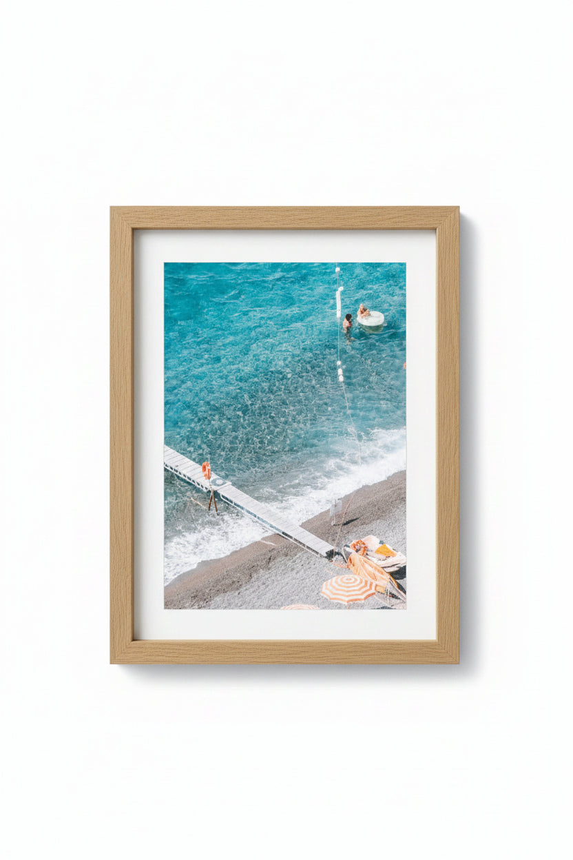 A framed photograph of a beach scene with people and umbrellas, matte board is white, and the frame is made of Tasmanian Oak.