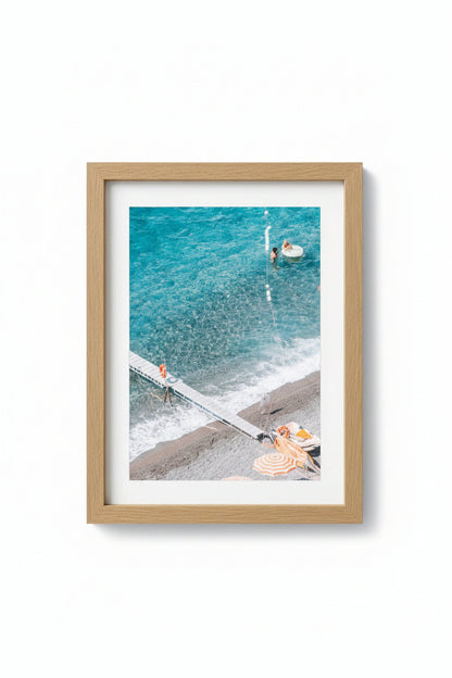 A framed photograph of a beach scene with people and umbrellas, matte board is white, and the frame is made of Tasmanian Oak.