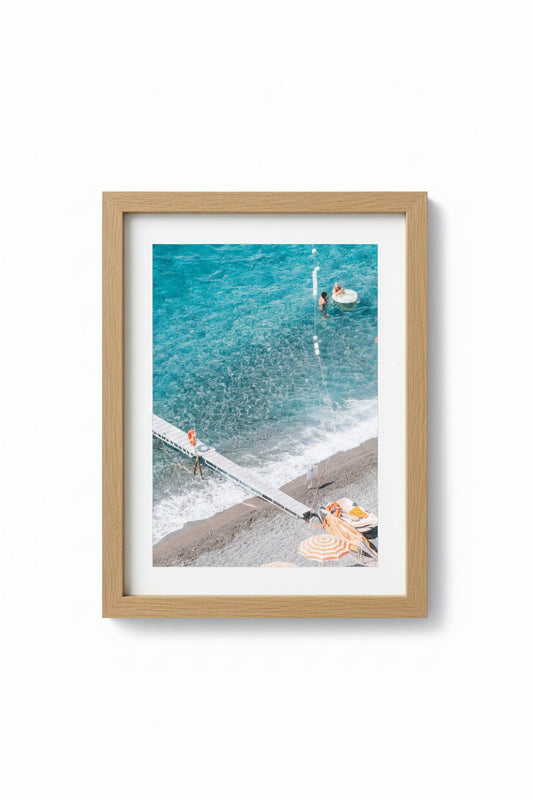 A framed photograph of a beach scene with people and umbrellas, matte board is white, and the frame is made of Tasmanian Oak.