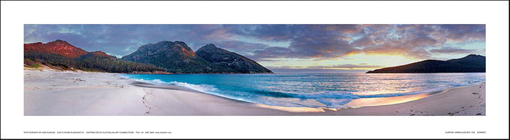 panoramic photograph of a beach scene at sunrise with mountains in the background, signed by Ken Duncan in silver foil on the bottom right.